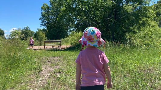 Two young girls exploring outdoors; running down a path in a restored prairie toward a large sand play area.